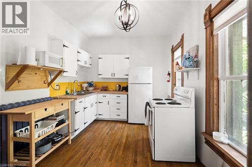 Kitchen featuring wood-finish flooring, white cabinetry with black hardware, and a bright yellow backsplash - 149 Young Street, Kitchener, ON - Indoor Photo Showing Kitchen With Double Sink