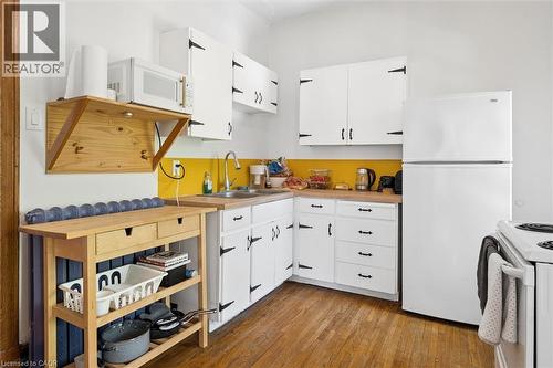 Kitchen featuring hardwood flooring, white cabinetry with black hardware, wood-finish countertops, and white appliances - 149 Young Street, Kitchener, ON - Indoor Photo Showing Kitchen With Double Sink