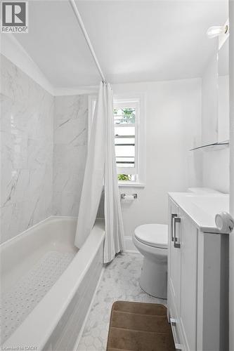 Bathroom featuring a built-in tub with tile surround, white hex tile flooring, white vanity with integrated sink, and an integrated wall mirror with shelf - 149 Young Street, Kitchener, ON - Indoor Photo Showing Bathroom