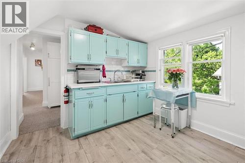 Kitchenette featuring light blue cabinetry, white countertops, a white subway tile backsplash with a decorative accent, wood-finish flooring, and natural light from two large windows - 149 Young Street, Kitchener, ON - Indoor Photo Showing Kitchen