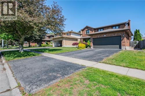Brick two-story residence featuring a dark garage door, paved driveway, mature front yard trees, and perimeter fencing - 141 Lynndale Road, Simcoe, ON 
