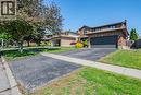 Brick two-story residence featuring a dark garage door, paved driveway, mature front yard trees, and perimeter fencing - 141 Lynndale Road, Simcoe, ON 