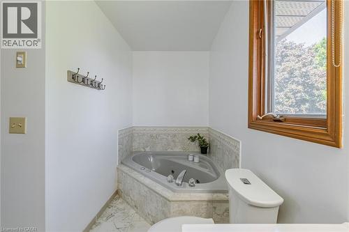 Corner jetted tub with tiled surround, wood-framed window, and white commode - 141 Lynndale Road, Simcoe, ON 