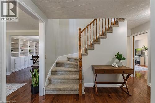Carpeted staircase with wooden banister, dark wood-finish flooring, white built-in shelving with lower cabinetry, and light gray wall paint - 141 Lynndale Road, Simcoe, ON 
