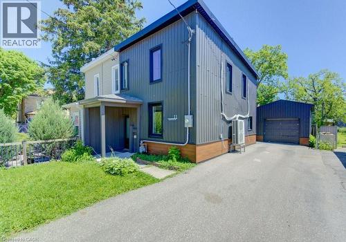 Modern-style residence featuring a dark corrugated metal exterior with wood-look trim, an attached covered entryway, a paved driveway, and a detached garage with a roll-up door - 11 Davidson Street, Cambridge, ON 