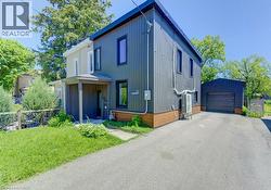 Modern-style residence featuring a dark corrugated metal exterior with wood-look trim, an attached covered entryway, a paved driveway, and a detached garage with a roll-up door - 