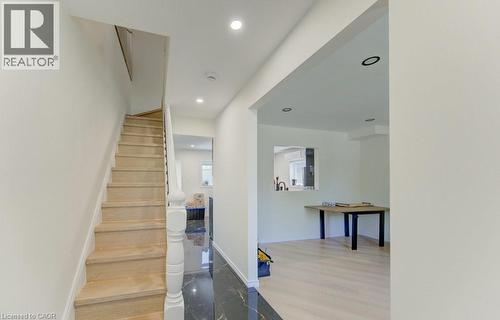 Open-concept interior featuring light wood-finish flooring, recessed lighting, a white painted staircase with a matching newel post, and a black marble-look tile entry - 11 Davidson Street, Cambridge, ON 