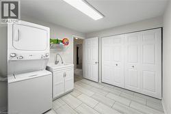 Dedicated laundry area featuring a stacked washer and dryer unit, utility sink with base cabinet, wire shelving, and light wood-finish flooring - 