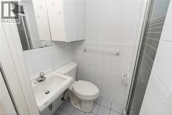 Bathroom featuring white wall tile, a wall-mounted sink, toilet, and a glass-enclosed shower - 