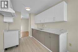 Galley kitchen featuring dual-toned cabinetry with light-colored upper cabinets and darker lower cabinets, light-colored countertops, and wood-finish flooring - 