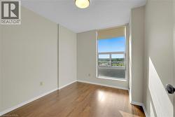 Bright room featuring wood-finish flooring, light-toned walls, and a large window with a roller shade - 