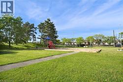 Expansive green space featuring a vibrant red and blue playground structure, multiple swing sets, and mature trees providing natural shade - 