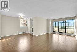 Spacious open-concept room featuring warm wood-finish flooring, neutral wall tones, and extensive natural light from a full wall of windows - 