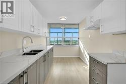 Galley kitchen featuring light wood-finish flooring, two-tone cabinetry with brushed nickel hardware, and stone-finish countertops - 