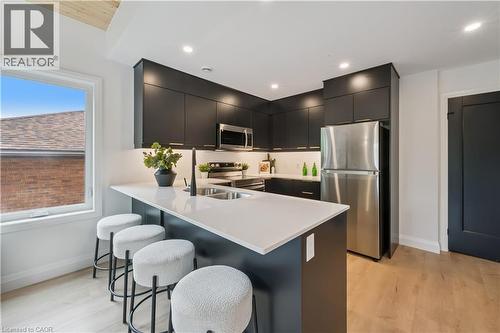 Contemporary kitchen with a central island featuring a white countertop and seating space, dark flat-panel cabinetry, stainless steel appliances, and light wood-finish flooring - 60 Arlington Boulevard Unit# 3, Kitchener, ON 