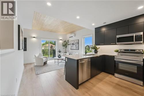 Contemporary kitchen featuring dark flat-panel cabinetry, stainless steel appliances, a white countertop, and wood-finish flooring - 60 Arlington Boulevard Unit# 3, Kitchener, ON 