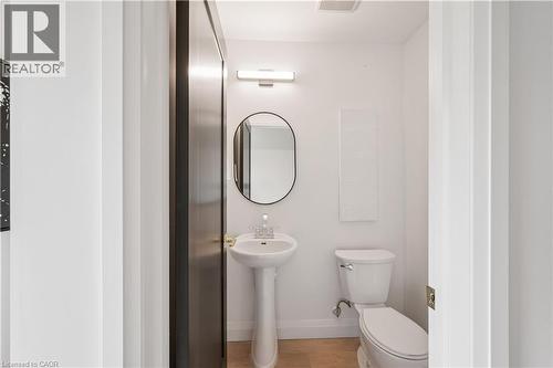 White-walled powder room featuring a pedestal sink with chrome faucet, a wall-mounted oval mirror, and a white toilet - 60 Arlington Boulevard Unit# 3, Kitchener, ON 