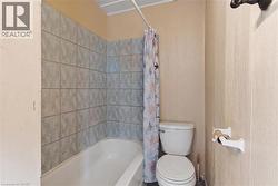Full bathroom featuring a white porcelain tub, light gray wall tile, and a built-in toilet - 