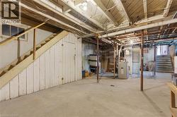 Concrete floor basement with exposed ceiling joists and support beams, featuring a wooden staircase with a partial railing - 
