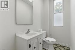 Bathroom featuring a white vanity with a ceramic basin, chrome faucet, wall-mounted mirror, and a window providing natural illumination - 