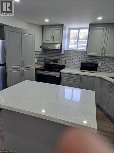 Modern kitchen featuring a spacious center island with a light-toned countertop, gray cabinetry, subway tile backsplash, stainless steel range with hood, and wood-finish flooring - 2240 Headon Road Unit# Lower, Burlington, ON 