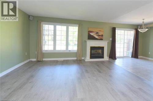 Living area featuring a fireplace with a white mantel, wood-finish flooring, and a large window - 2 Harbour Drive Unit# 17, Stoney Creek, ON 