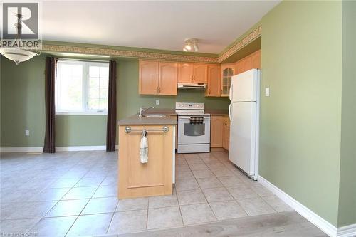 Open-concept kitchen featuring light wood cabinetry, white appliances, a peninsula with an integrated sink, and ceramic tile flooring - 2 Harbour Drive Unit# 17, Stoney Creek, ON 