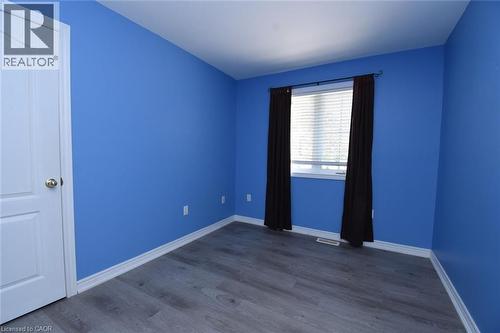Room featuring vibrant blue walls, light wood-finish flooring, white trim, and a white interior door with a gold-tone knob - 2 Harbour Drive Unit# 17, Stoney Creek, ON 