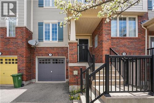 Brick and siding townhouse exterior featuring a covered front entry, concrete stairs with black metal railings, a single-car garage with a panel door, and white-framed windows with dark shutters - 7 Hepworth Crescent, Ancaster, ON 