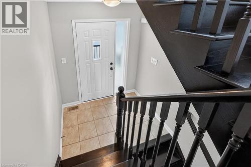 Entry foyer featuring a paneled door with frosted sidelight, ceramic tile flooring, and a dark wood-finish staircase with balusters - 7 Hepworth Crescent, Ancaster, ON 