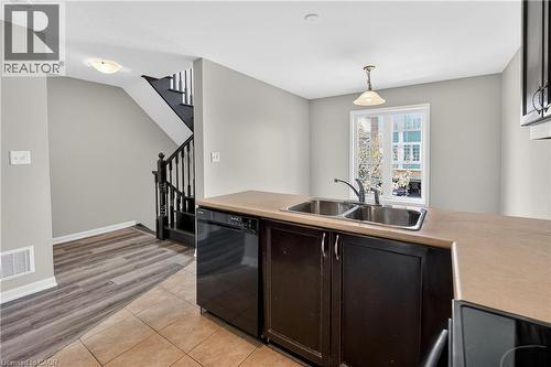 Kitchen counter with dual stainless steel sink, built-in dishwasher, and dark wood-finish cabinetry - 7 Hepworth Crescent, Ancaster, ON 