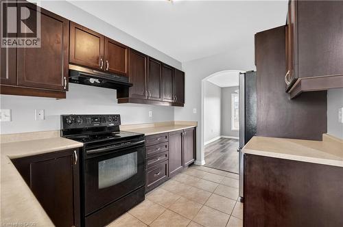 Efficient kitchen featuring dark wood-finish cabinetry, light-toned countertops, and a black electric range with an overhead vent - 7 Hepworth Crescent, Ancaster, ON 