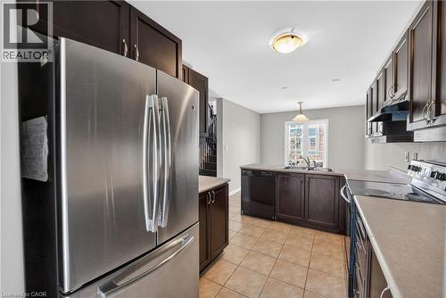 Kitchen featuring dark wood cabinetry, stainless steel appliances, light-toned countertops, tile flooring, and a pendant light fixture - 7 Hepworth Crescent, Ancaster, ON 