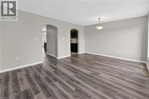 Spacious room featuring wood-finish flooring, light grey wall tones, white trim, and arched doorways - 7 Hepworth Crescent, Ancaster, ON 