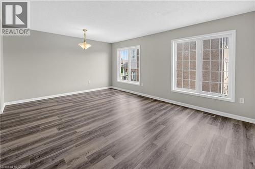 Spacious room featuring wood-finish flooring, light gray walls, white trim, and multiple large windows with grids - 7 Hepworth Crescent, Ancaster, ON 