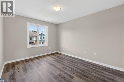 Neutral-toned room featuring a large window, light-colored walls, wood-finish flooring, white trim, and a ceiling-mounted light fixture - 7 Hepworth Crescent, Ancaster, ON 
