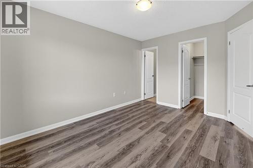 Spacious room featuring wood-finish flooring, light neutral wall paint, white trim, and a ceiling-mounted light fixture - 7 Hepworth Crescent, Ancaster, ON 