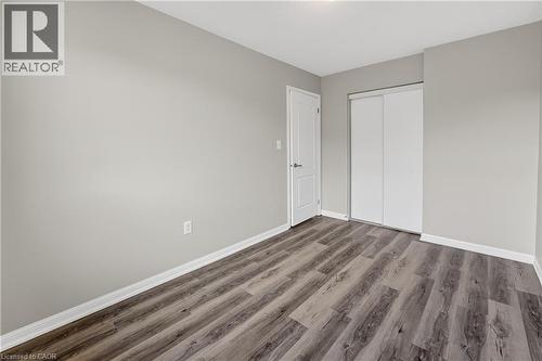 Spacious room featuring wood-finish flooring, light gray wall paint, white baseboards, a white interior door, and a closet with white sliding doors - 7 Hepworth Crescent, Ancaster, ON 
