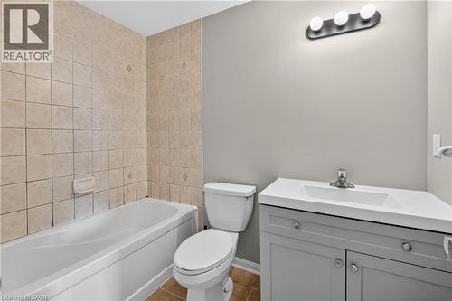 Full bathroom featuring a white tub, square beige wall tiling, a white toilet, and a vanity with a white countertop, integrated sink, and gray cabinetry - 7 Hepworth Crescent, Ancaster, ON 