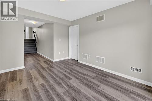 Spacious room featuring wood-finish flooring, light grey painted walls, white baseboards, and a white two-panel interior door - 7 Hepworth Crescent, Ancaster, ON 