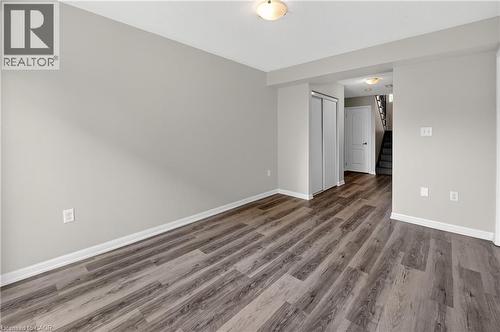 Spacious room featuring wood-finish flooring, light grey walls, white baseboards, and two flush-mount ceiling lights - 7 Hepworth Crescent, Ancaster, ON 