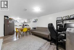 Open-concept living area featuring wood-finish flooring, a full kitchen with white cabinetry and a built-in range hood, and recessed lighting - 