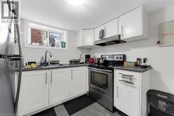 Compact kitchen featuring white cabinetry, dark countertops, stainless steel appliances, and a window - 