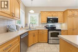 Kitchen featuring light wood cabinetry, a corner sink with a window, stainless steel appliances, and tile flooring - 
