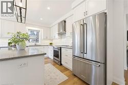 Modern kitchen featuring white shaker cabinetry, stainless steel appliances, a kitchen island with stone countertop, wood-finish flooring, and a subway tile backsplash - 