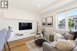 Living area featuring wood-finish flooring, recessed lighting, and a large window with roller shades - 