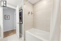 Bathroom featuring a white soaking tub, light-toned horizontal tiled shower surround, and white tile flooring - 