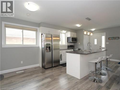 Kitchen featuring wood-finish flooring, white cabinetry, dark countertops, and stainless steel appliances - 771 Monsarrat Avenue, London, ON 