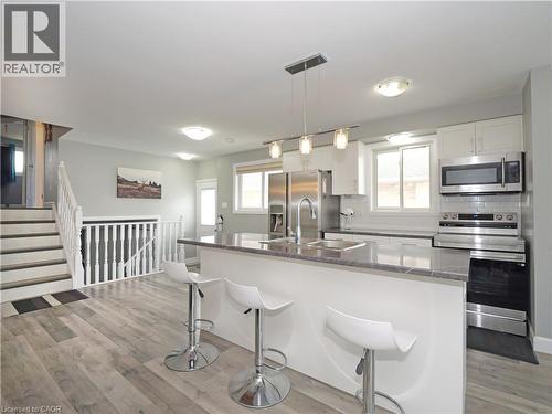 Open-concept kitchen featuring an island with stone-finish countertop, stainless steel appliances, white cabinetry, and wood-finish flooring - 771 Monsarrat Avenue, London, ON 
