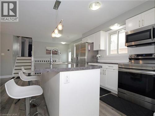 Modern kitchen featuring an island with an undermount sink, stainless steel appliances, white cabinetry, and wood-finish flooring - 771 Monsarrat Avenue, London, ON 
